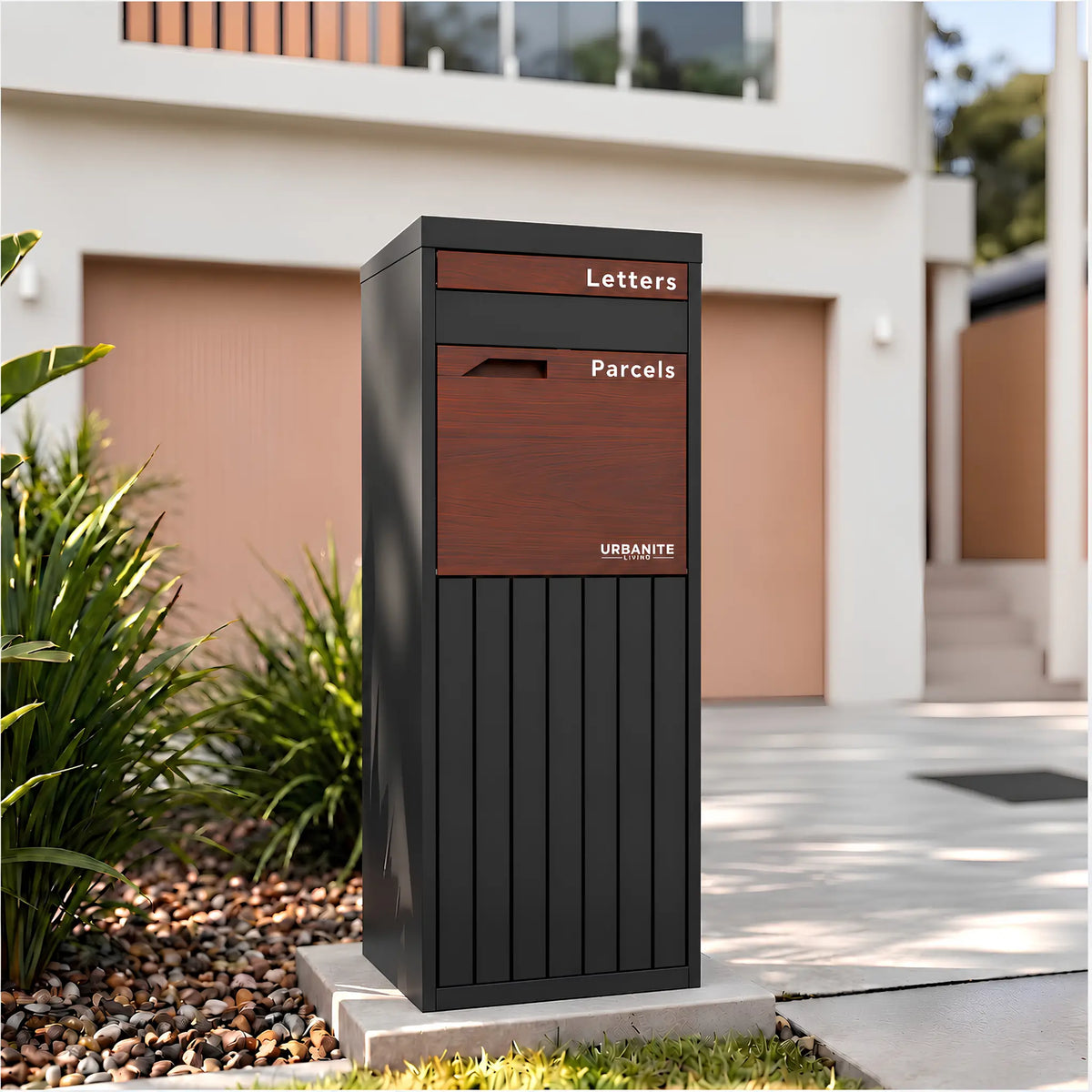 Urbanite Living Corella Extra Tall freestanding parcel letterbox in charcoal with dark wood look metal front panels beside a driveway at a home.