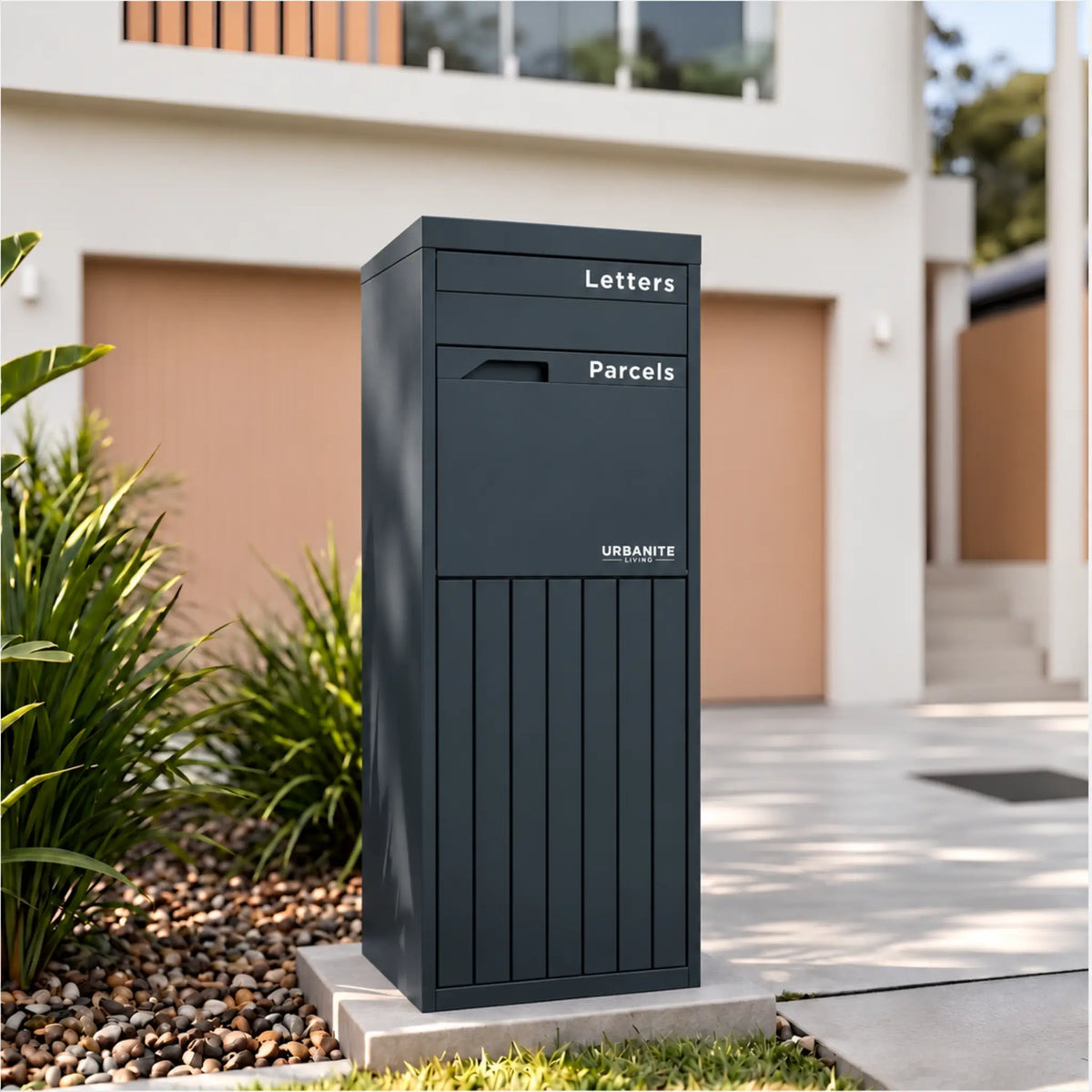 Urbanite Living Corella Extra Tall freestanding parcel letterbox in charcoal beside a driveway at a home.