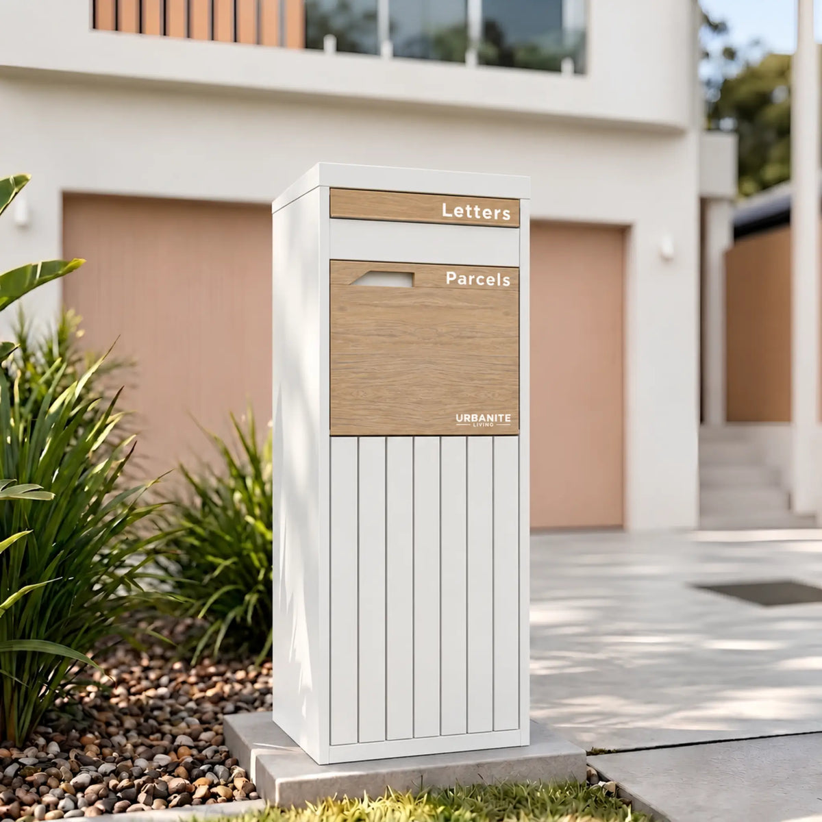 Urbanite Living Corella Extra Tall freestanding parcel letterbox in white with light wood look metal front panels beside a driveway at a home.
