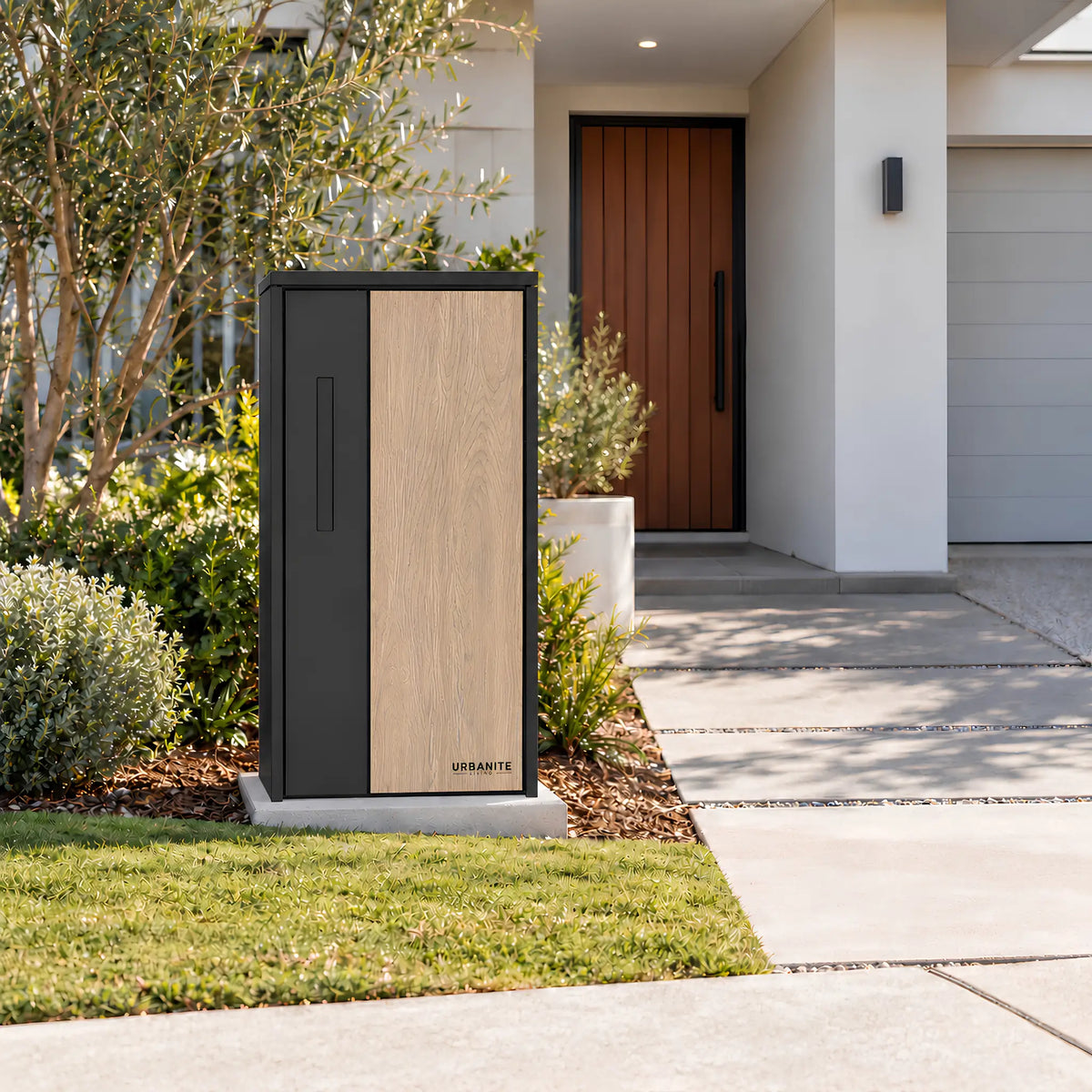 Urbanite Living The Don Extra Wide Parcel Letterbox in black with light wood look metal front panel beside a landscaped front path. 