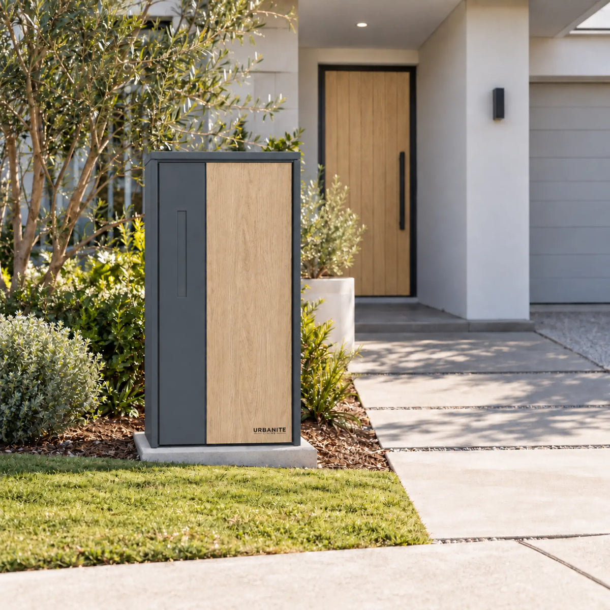 Urbanite Living The Don Extra Wide Parcel Letterbox in charcoal with light wood look metal front panel beside a landscaped front path. 