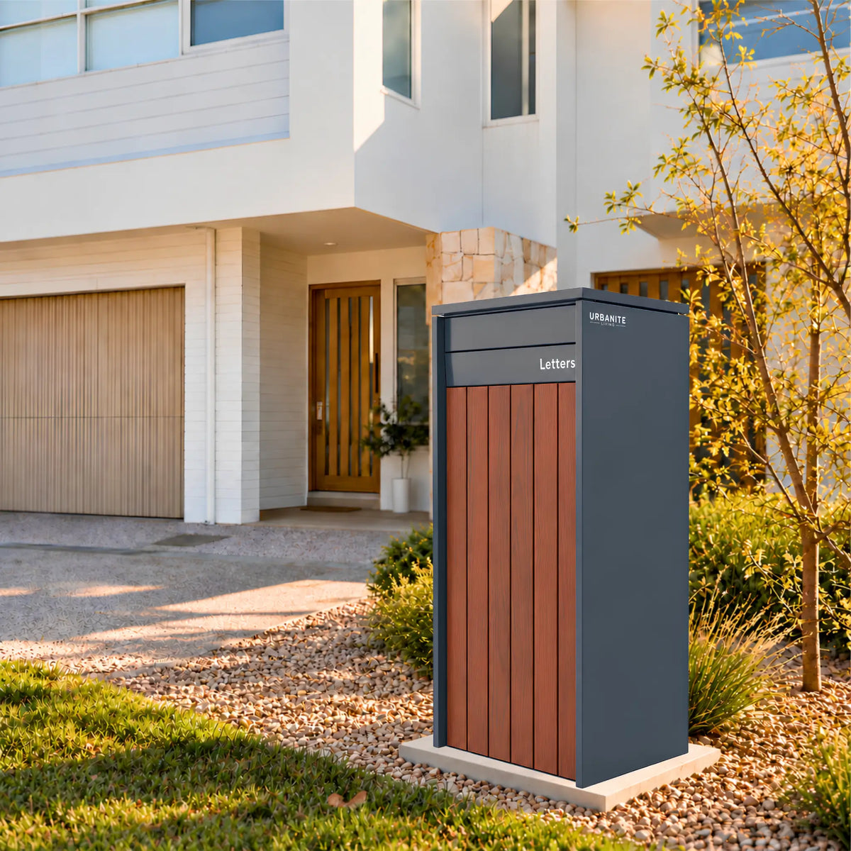 Heron Extra Wide parcel letterbox in charcoal with dark wood front panels in the front garden of a two-storey home - Urbanite Living.