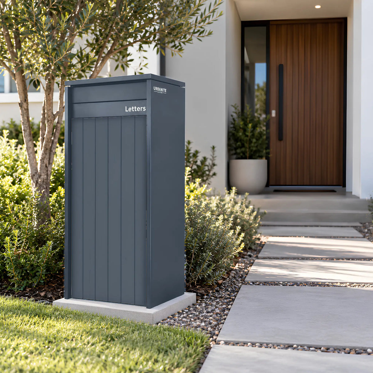 Urbanite Living Heron Extra Wide freestanding parcel letterbox in a charcoal finish beside a garden path.