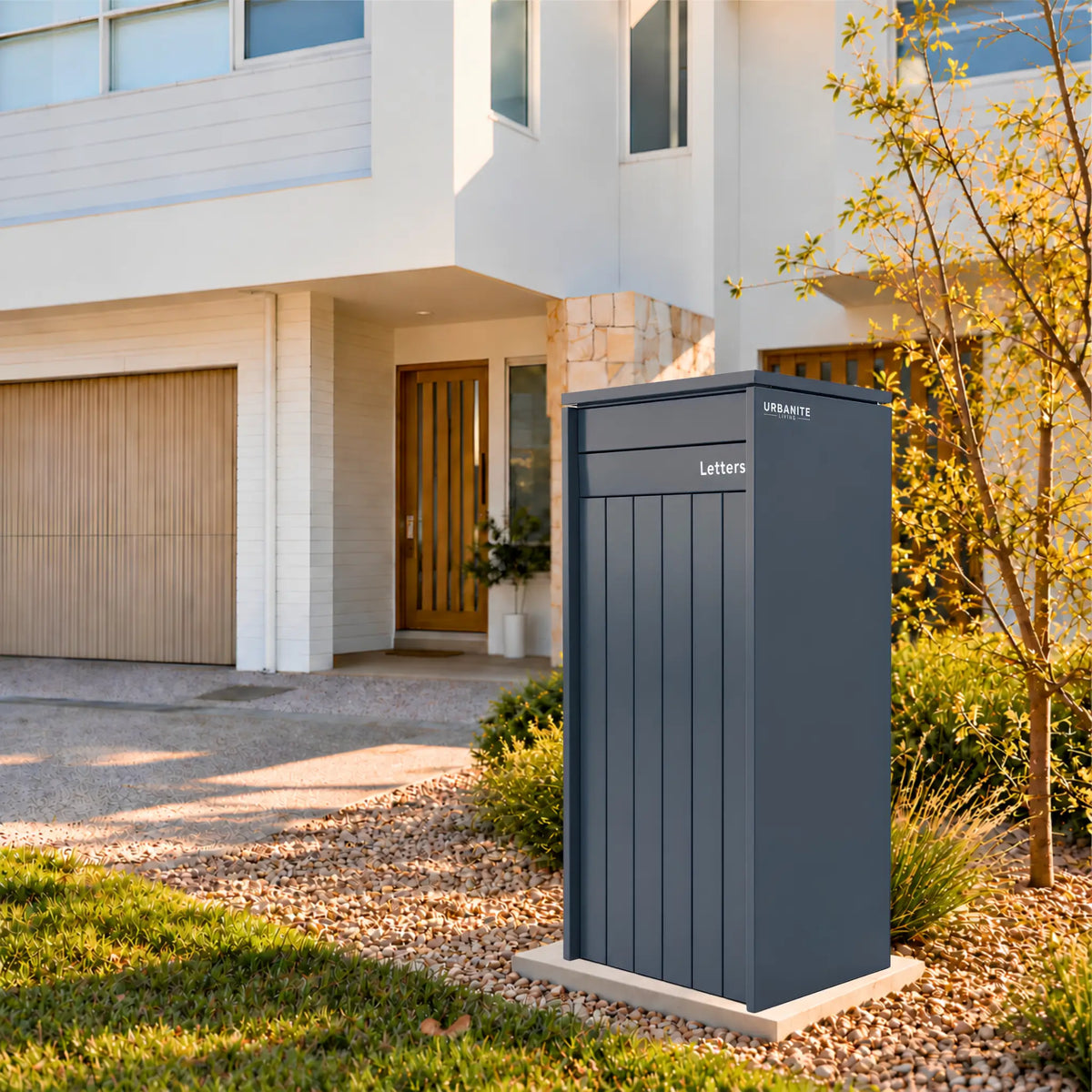 Urbanite Livings Heron Extra Wide parcel letterbox in a charcoal finish in the front garden of a two-storey home.