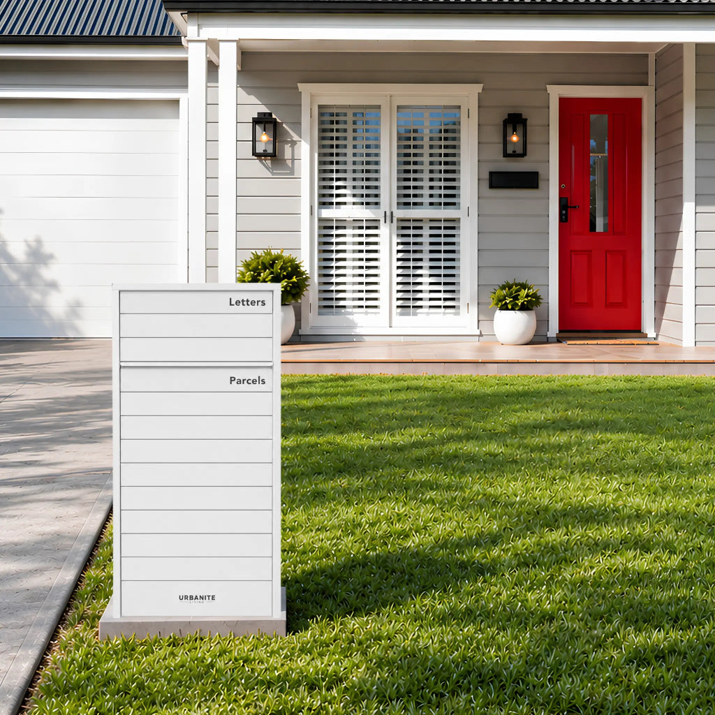 Urbanite Living Kestrel freestanding parcel letterbox in white on a front lawn beside a driveway.