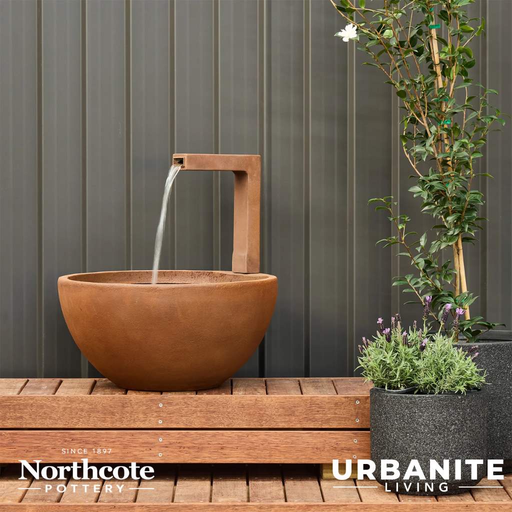 Iron rust coloured patio pond with flowing water sitting on a timber deck.