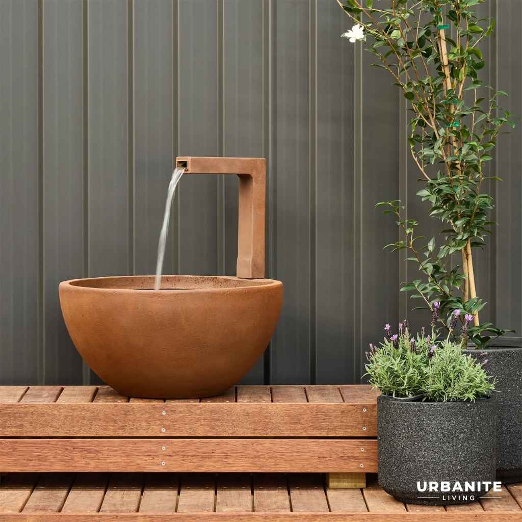 Iron rust coloured patio pond with flowing water sitting on a timber deck.