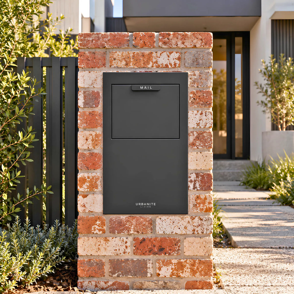 Urbanite Living Wren parcel letterbox in black, built into a red brick pillar at a home's front entrance.